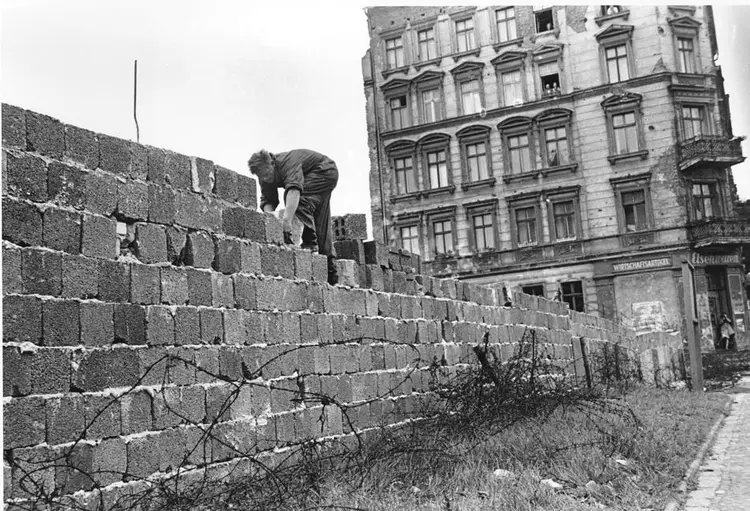 An East Berlin policeman puts bricks in place as the Berlin Wall is heightened to 15 feet, 5 m, separating East and West Berlin, Germany, on Sept. 9, 1961. People watch from their apartment building windows in background above. (AP Photo)