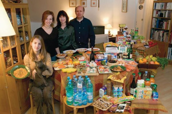 FRA04.0001.xxf1rw (MODEL RELEASED IMAGE) The Le Moine family in the living room of their apartment in the Paris suburb of Montreuil, with a week’s worth of food. Michel Le Moine, 50, and Eve Le Moine, 50, stand behind their daughters, Delphine, 20 (standing), and Laetitia, 16 (holding spaghetti and Coppelius the cat). Cooking methods: electric stove, microwave oven. Food preservation: refrigerator-freezer. Favorite foods—Eve: fresh vegetables. Delphine: Thai food. Laetitia: pasta carbonara. /// The Le Moine family is one of the thirty families featured in the book Hungry Planet: What the World Eats (p. 124). Food expenditure for one week: $419.95 USD. (Please refer to Hungry Planet book p. 125 for the detailed food list.)