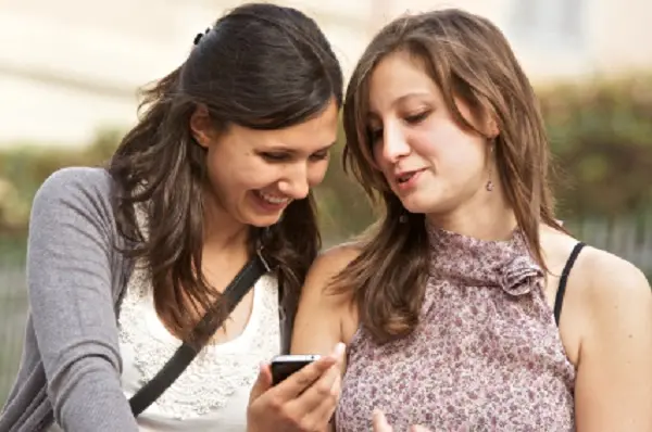 Two girlfriends in park with a mobile phone