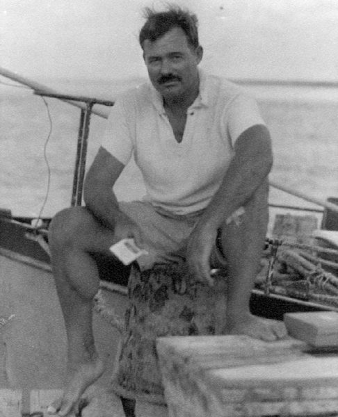 EH6670P 1930s Ernest Hemingway sitting on a dock next to the Pilar, 1930s. Photographer unknown in the Ernest Hemingway Collection of the John F. Kennedy Presidential Library and Museum, Boston.