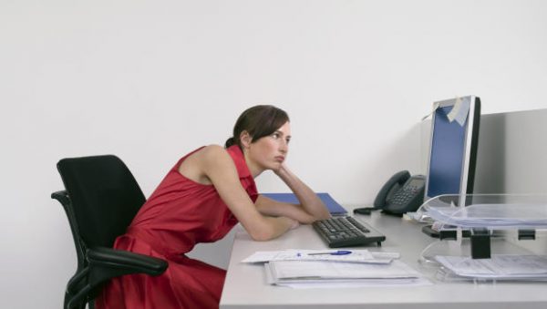 Side view of a bored female office worker looking at notes on computer monitor at desk