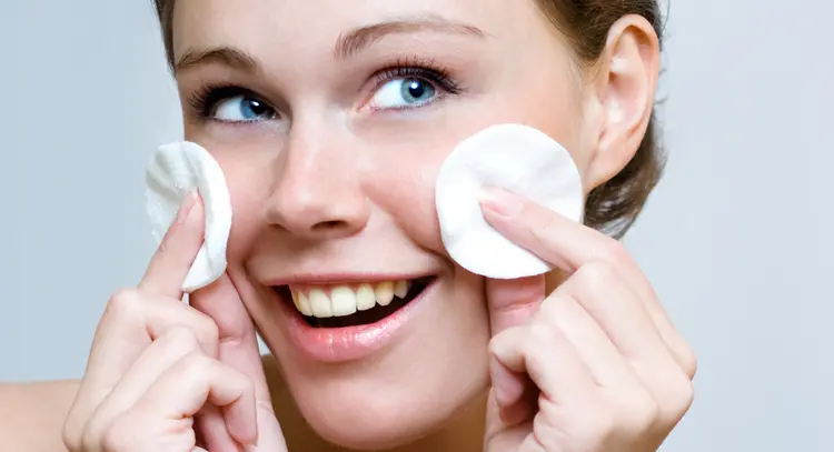 Woman cleaning face by cotton pad