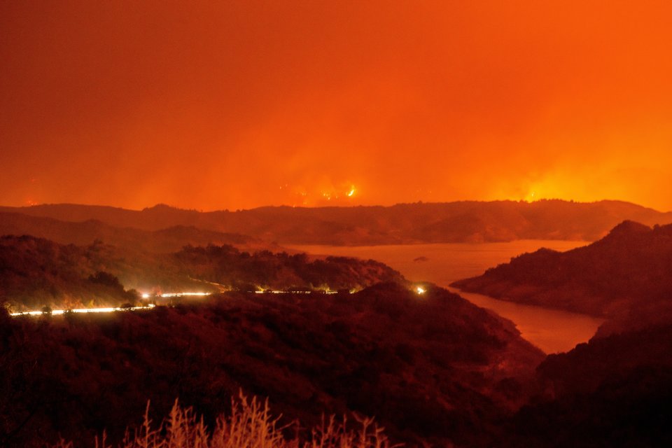 CALIFORNIA, USA - DECEMBER 5: Cars drive around Lake Casitas and away from the Thomas Fire as it crests a mountains near the lake on December 5, 2017 in Ventura, California, United States. The fire has consumed over 50,000 acres according to the California Department of Forestry and Fire protection. (Photo by Justin L. Stewart/Anadolu Agency/Getty Images)